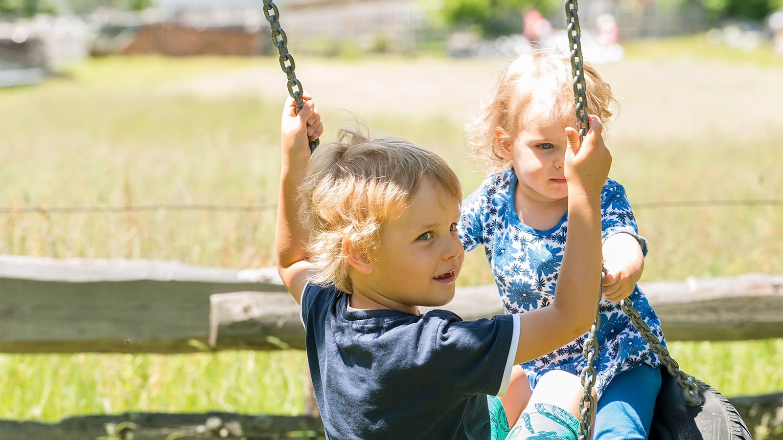 zwei kleine Kinder beim Schaukeln auf dem Kinderspielplatz des Hotels Alpenfrieden