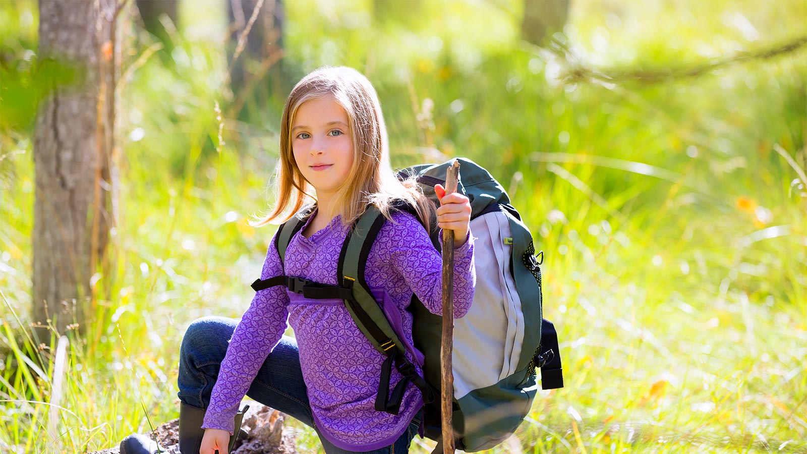una bambina durante un'escursione in montagna con zaino e bastone