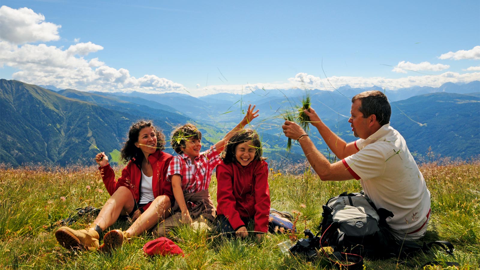 una famiglia seduta su un prato fiorito d'estate nell'area sci e malghe Rio Pusteria