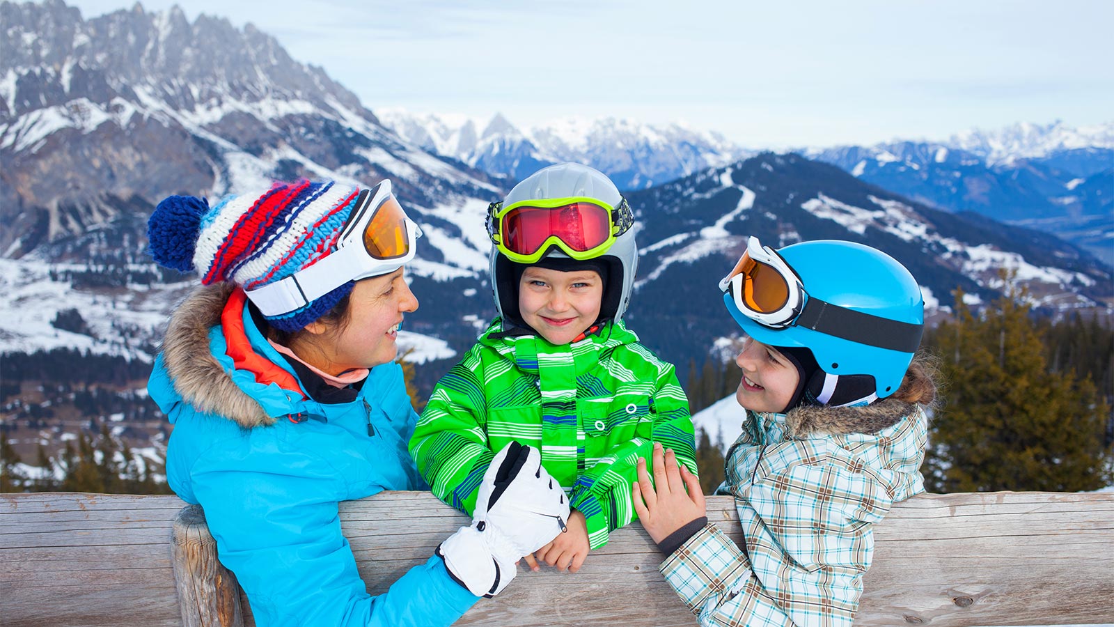 eine Mutter und zwei Kinder sitzen auf einer Bank auf der Skipiste und haben Spaß